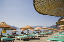 Marmaris on the Turkish Riviera in early Summer season.  Lines of parasols and sunbeds for rent on the beach in morning sun. coastcoastalresortholidayholidaymakerssunrelaxingleisuresuntansun...