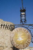 Rhodes Town.  Hanging  circular cafe sign in the Old Town against stone wall of ancient gate and cloudless blue sky.AegeancoastcoastalFormer Ottoman territoryearlySummer seasonlocation of Guns...