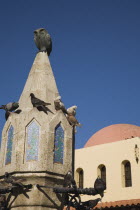 Rhodes Town.  Part seen fountain in Argykastron Square in the Old Town with pigeons perched around it and red domed roof of building behind. AegeancoastcoastalFormer Ottoman territoryearlySummer...