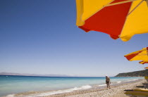 Ixia beach outside Rhodes Town.  Part seen red and yellow sun umbrellas on beach in late afternoon sun on perfect clear day with tourist walking along shoreline.GreekAegeanCoast - CoastalRodiPack...