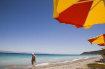 Ixia beach outside Rhodes Town.  Part seen red and yellow sun umbrellas on beach in late afternoon sun on perfect clear day with tourist walking along shoreline.GreekAegeanCoast - CoastalRodiPack...