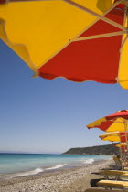 Ixia beach outside Rhodes Town.  Part seen red and yellow sun umbrellas and line of sun loungers on beach in late afternoon sun on perfect clear day.GreekAegeanCoast - CoastalRodiPackage holiday...