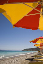 Ixia beach outside Rhodes Town.  Part seen red and yellow sun umbrellas and line of sun loungers on beach in late afternoon sun on perfect clear day.GreekAegeanCoast - CoastalRodiPackage holiday...