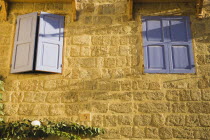 Exterior wall of stone  Greek village style house with blue painted wooden window shutters.AegeanGreekByzantineRodilocation for Guns of Navaronecoast coastalsun sunshine sunny holidayresortd...