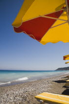 Ixia beach resort popular for water sports with part seen red and yellow striped sun umbrella in foreground against backdrop of cloudless sky and distant Turkish coast on bright summer morning.Aegea...