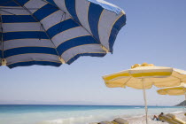 Ixia beach resort popular for water sports with part seen blue  white and yellow striped sun umbrellas and sun loungers in foreground against blue  cloudless sky and sea view.AegeanRodiseacoast co...