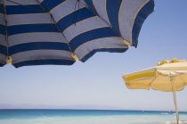 Ixia beach resort popular for water sports with part seen blue  white and yellow striped sun umbrellas in foreground against blue  cloudless sky and sea view.AegeanRodiseacoast coastalpackage hol...