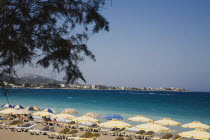 xia beach resort popular for water sports with line of brightly coloured striped sun umbrellas and sun loungers overlooking deep aquamarine water and coastline.AegeanRodiseacoast coastalpackage h...