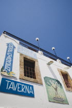 Lindos.  Traditional Blue and White painted exterior of local taverna with painted signs advertising rooftop cafe. AegeanGreekSummer seasonRodicoast coastalpackage holidaytrip destinationDesti...