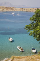 Lindos.  Looking down on shallow bay with moored boats  in high summer season with view north along coastline and part view of tree in foreground.Greek IslandsAegeanRodicoast coastalseaswimbath...