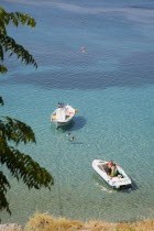 Lindos.  Looking down on shallow bay with moored boats  and tourists swimming in high summer season.Greek IslandsAegeanRodicoast coastalseaswimbathingresortholidaypackagetripDestination De...