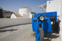 Lindos.  Classic Greek Island scene with bright blue delivery motorbike in foreground of whitewashed church on paved stone path in bright afternoon sunshine.Greek IslandsAegeanRodicoast coastalse...