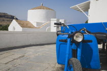 Lindos.  Classic Greek Island scene with bright blue delivery motorbike in foreground of whitewashed church on paved stone path in bright afternoon sunshine.Greek IslandsAegeanRodicoast coastalse...