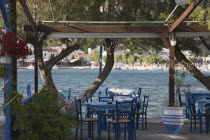 Pythagorio.  Greek restaurant with tables and chairs beneath canopy overlooking bay in early summer season.AegeanGreek IslandsPythagorionharbour Summerseacoast coastalresortholidaypackagetr...