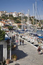 Pythagorio.  Tourists walking along waterfront with line of moored rental yachts and cafes overlooking boats in early Summer season.AegeanGreek IslandsPythagorionSummerseacoast coastalresortho...