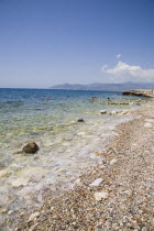 Pythagorio.  Tourists swimming in clear water on pebble beach with South West coast of island in distance behind.AegeanGreek IslandsPythagorionSummerseacoast coastalresortholidaypackagetrip...