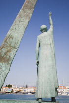 Pythagorio.  Statue of the philosopher and mathematician Pythagoras on waterfront with diagrams on angled plinth alongside framing view across harbour to line of waterfront buildings beyond.AegeanGr...