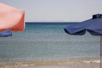 Pythagorio.  Red and blue beach parasols with flat calm sea and cloudless  hazy blue sky in early Summer season.North Eastern AegeanGreek IslandsPithagorion Pythagorioncoast coastalseaSummerpac...