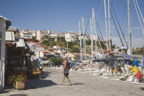 Pythagorio.  Female tourist on waterfront with line of moored rental yachts overlooked by cafes in early Summer season June.  Houses on hillside beyond.North Eastern AegeanGreek IslandsPithagorion...