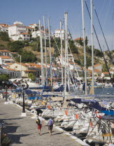 Pythagorio.  Tourists on waterfront with line of moored rental yachts overlooked by cafes in early Summer season June.  Houses on hillside beyond.North Eastern AegeanGreek IslandsPithagorion Pythag...