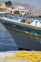 Yialos harbour  main port of Symi island.  Blue and white painted fishing boat moored beside jetty with yellow fishing nets in foreground and waterfront houses behind. AegeanGreek IslandsSimicoast...