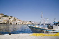 Yialos harbour  main port of Symi island.  Blue and white painted fishing boat moored beside jetty with yellow fishing nets in foreground and waterfront houses behind. AegeanGreek IslandsSimicoast...