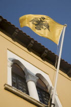 Yialos.  Yellow flag depicting crowned  sword bearing  double headed eagle  the emblem of the Byzantine empire flying from window of yellow and white painted building.AegeanGreek IslandsSimicoast...