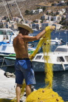 Yialos.  Fisherman working with bright yellow nets on the harbourside with moored boats beyond.AegeanGreek IslandsSimicoast coastalseaSummerpackageholidayresortvacationtripdestinationDest...