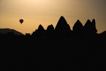 Turkey, Cappadocia, Goreme, Hot air balloons in flight over landscape, Silhouette of rock shapes with hot air balloon in the distance.