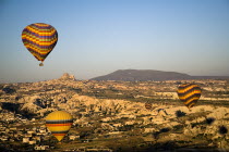 Turkey, Cappadocia, Goreme, Hot air balloons in flight over landscape, Hot air balloons in flight over landscape in early morning sunlight with Uchisar town in background.