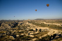 Turkey, Cappadocia, Goreme, Hot air balloons in flight over landscape, Hot air balloons in flight in early morning sunlight with Uchisar town in background and Goreme to the left.