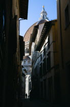 ITALY, Tuscany, Florence, The Dome of the Cathedral of Santa Maria del Fiore the Duomo by Brunelleschi and marble sides of the church seen down a narrow street with people walking past.