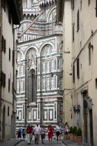 ITALY, Tuscany, Florence, The Cathedral of Santa Maria del Fiore with the marble sides of the church seen down a narrow street with people walking past.