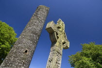 IRELAND, County Louth, Monasterboice Monastic Site, the West Cross slanted angular view of the east face with Round Tower in the background. 