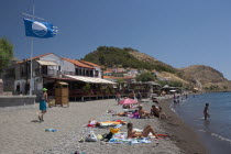 GREECE, North East Aegean, Lesvos Island, Eresos, View of beach with people sunbathing and swimming just in front of the villages bars and restaurants.