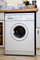 Architecture, Interiors, machinery, White domestic washing machine household appliance set under worktop in utility laundry room.