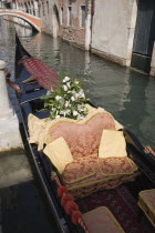 Italy, Veneto, Venice, Gondola prepared for wedding with red and gold brocade seating and flowers, moored at canal jetty.