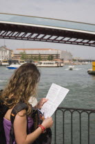 Italy, Veneto, Venice, Female tourist looking at map in front of Ponte di Calatrava Bridge, the fourth bridge built across the Grand Canal opened in September 2008 linking the train station and Piazza...