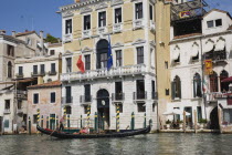 Italy, Veneto, Venice, Gondolier steers gondola from Rialto bridge along Grand Canal with Venice Republic, EU and Italian tricolour flags on the facades of buildings behind.