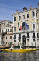 Italy, Veneto, Venice, Female pair taking part in Regata Storica Venice Regatta rowing yellow gondola on the Grand Canal passing waterside buildings with Venice Republic, EU and Italian tricolour flag...