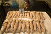 Greece, Attica, Athens, Central Market, Fresh squid displayed on stall with male shopkeeper standing behind.