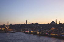 Turkey, Istanbul, Sultanahmet, The Golden Horn. The New Mosque or Yeni Camii at left, the Galata Bridge, and Suleymaniye Mosque at right with lights and advertising illuminated at dusk.