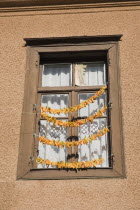 Turkey, Aydin Province, Kusadasi, Strings of yellow and orange chili peppers hanging from wooden window frame of house in the old town to dry in the summer sunshine.