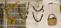 Turkey, Aydin Province, Kusadasi, Strings of chili peppers and mushrooms hanging in front of windows of whitewashed houses in the old town to dry in summer sunshine. Woven basket hanging at side.