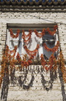 Turkey, Aydin Province, Kusadasi, Strings of red and orange chilies hung up to dry in late afternoon summer sunshine across windows of whitewashed houses in the old town casting shadows over the brick...