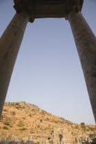 Turkey, Izmir Province, Selcuk, Ephesus, Pair of marble columns supporting roof framing ruins scattered across hillside in antique city of Ephesus on the Aegean sea coast.