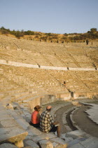 Turkey, Izmir Province, Selcuk, Ephesus, Tourist couple sitting in amphitheatre in the antique city of Ephesus on the Aegean sea coast.