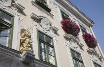 Austria, Vienna, Pastel painted building facade with religious statue and colourful window boxes of pink flowers.