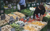 Austria, Vienna, The Naschmarkt, Stallholder selecting mushrooms from display of fresh produce also including potatoes, ginger, cucumbers and squash.