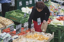 Austria, Vienna, The Naschmarkt, Stallholder selecting mushrooms from display of fresh produce also including potatoes, ginger, cucumbers and squash.